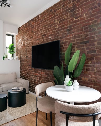 Modern living room with exposed brick wall, wall-mounted TV, beige sofa, white oval table, and potted cactus plant