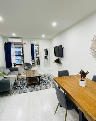 Modern open-plan living and dining area with wood table, gray sofa, potted plants, and wall-mounted TV
