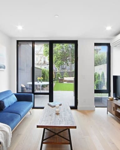 Modern living room with blue sofa, wooden coffee table, TV stand, and glass doors opening to garden patio