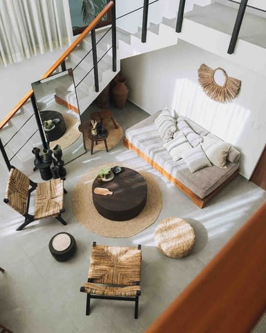 Overhead view of modern loft bedroom with bed, woven seating, round black table, and staircase with wooden railing