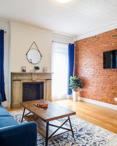 Living room with blue sofa, exposed brick wall, fireplace, TV, and hardwood floors