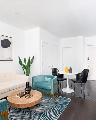 Modern living room with cream sofa, turquoise chairs, round wood coffee table, abstract wall art, and potted plants