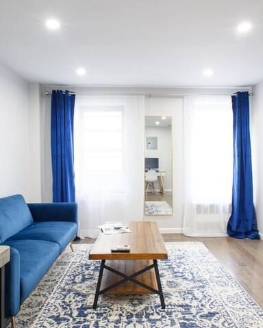 Modern living room with blue sofa, wooden coffee table, wall-mounted TV, and blue curtains