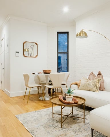 Modern studio apartment with white brick walls, cream sofa, round dining table, wooden floors, and brass arc lamp