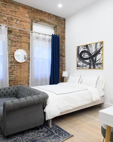 Modern bedroom with exposed brick wall, white bed, gray armchair, and blue curtains