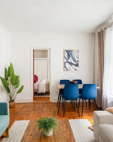 Bright open-plan living room with turquoise sofa, blue dining chairs, wooden floors, and modern artwork on white walls