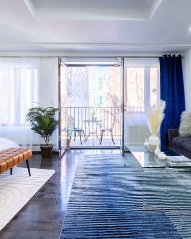 Modern studio apartment with bed, dark sofa, glass coffee table, and balcony overlooking city buildings