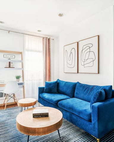 Modern living room with blue velvet sofa, round wooden coffee table, and abstract line art above seating area