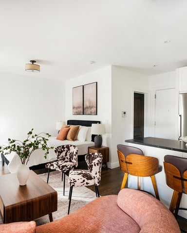 Open-plan studio with kitchen, living area, bed, and seating with mid-century modern furnishings and white walls
