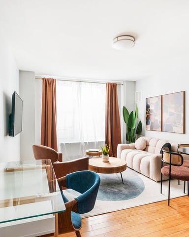 Modern living room with round mirror, cream sofa, blue armchair, orange curtains, and wood flooring