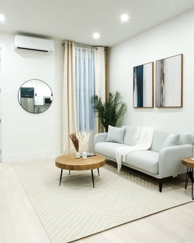Modern living room with white sofa, round wood coffee table, potted plants, circular mirror, and framed wall art