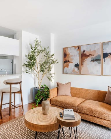 Open-plan living room with mustard sofa, wooden coffee tables, kitchen with bar seating, and abstract wall art