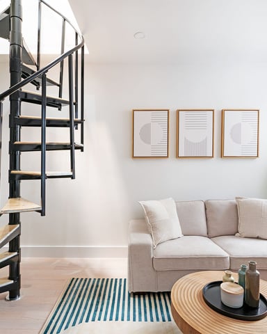 Modern living room with spiral staircase, beige sofa, wood coffee table, and potted plant