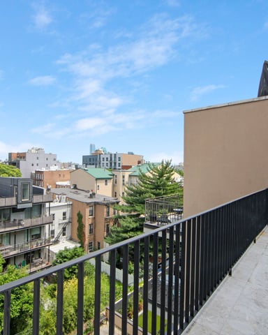 Rooftop terrace with black metal railing overlooking urban neighborhood with mixed residential buildings and green trees