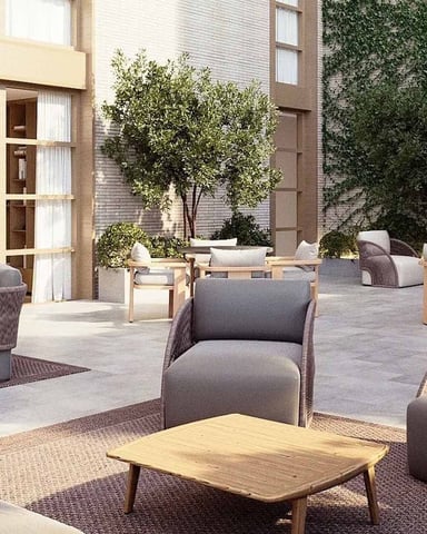 Courtyard with woven lounge chairs, wooden tables, potted plants, and ivy-covered brick buildings