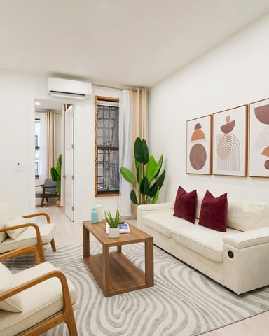 Bright living room with cream sofa, wooden armchairs, abstract wall art, potted plants, and wall-mounted TV