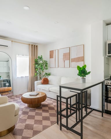 Open-plan studio with cream armchairs, kitchen with stainless steel appliances, and checkered area rug