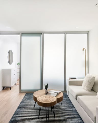 Modern studio apartment with cream sofa, wooden coffee table, desk with TV, and glass doors opening to balcony