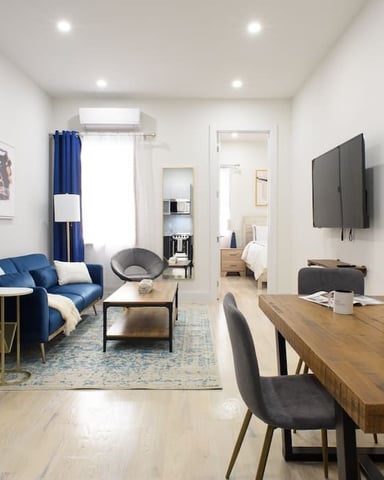 Open-plan living and dining area with blue sofa, wooden dining table, wall-mounted TV, and modern furnishings