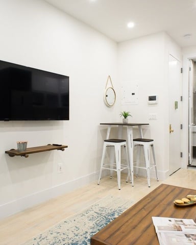 Modern open-plan kitchen and living room with wall-mounted TV, bar seating, stainless steel range, and light wood flooring.