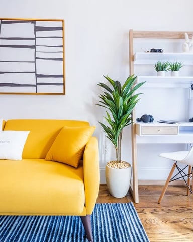 Bright studio with yellow sofa, white shelving unit, potted plant, and blue curtains on wooden floor