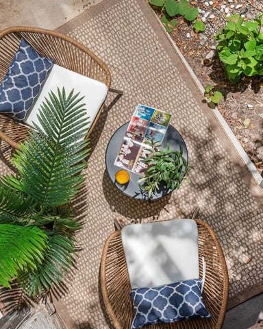 Overhead view of small patio with woven chairs, cushions, potted plants, and magazines on round table
