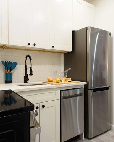Modern kitchen with white cabinetry, stainless steel appliances, black countertops, subway tile backsplash, and fresh citrus on cutting board