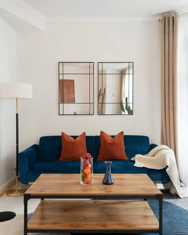 Bright living room with navy blue sofa, orange pillows, wooden coffee table, and framed mirrors on white walls