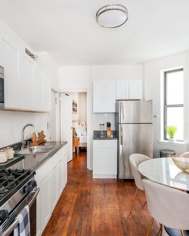 Modern kitchen with white cabinets, stainless steel appliances, gas range, marble dining table, and hardwood floors
