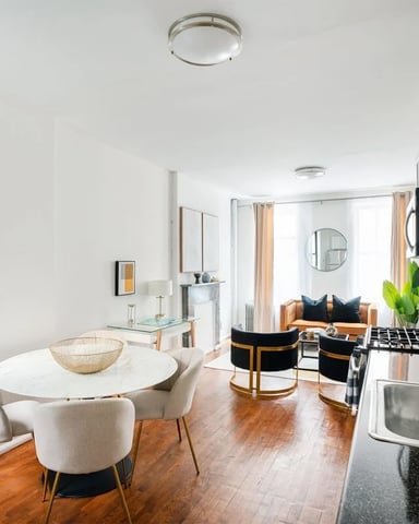 Open-plan kitchen and dining area with white cabinetry, stainless steel appliances, round white dining table, and living room with tan sofa visible beyond.