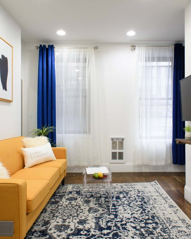 Modern living room with yellow sofa, wall-mounted TV, blue curtains, and framed abstract artwork