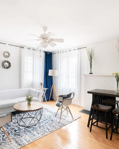 Bright open-plan living room with white sofa, round coffee table, black bar counter with stools, and hardwood floors throughout.