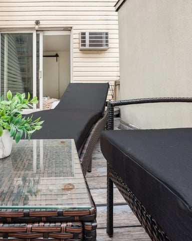 Patio with wicker lounge chairs, potted plant, and glass table overlooking residential building entrance