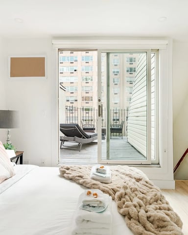 Bedroom with green upholstered headboard and glass doors opening to balcony overlooking city buildings