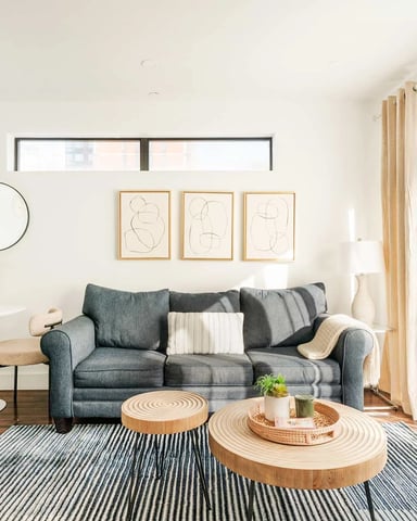 Bright living room with gray sofa, wooden coffee tables, striped rug, and three framed line drawings above the couch