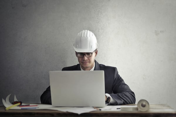Construction manager in hard hat and business suit working on laptop at desk with blueprints