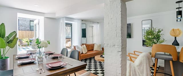 Open-plan dining and living room with wood table, leather sofa, black-and-white tile floor, and glass doors opening to patio.