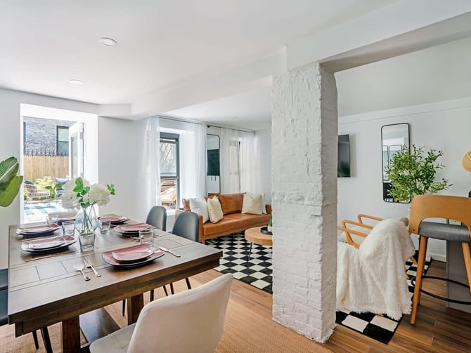 Open-plan dining and living room with wood table, leather sofa, black-and-white tile floor, and glass doors opening to patio